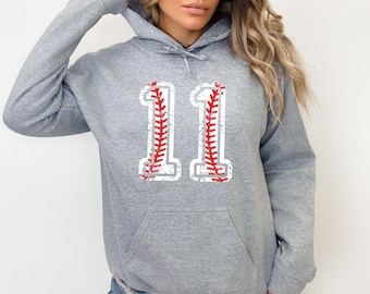 May include: Gray hooded sweatshirt with a white baseball number "11" with red stitching. The number has a distressed look.