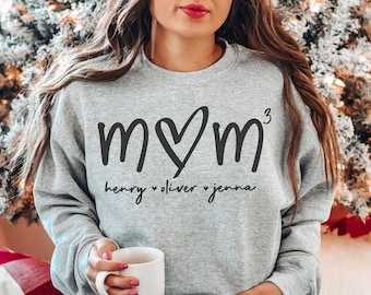 May include: A gray sweatshirt with the text "MOM" in black with a heart in place of the "O". The number "3" is written in superscript to the right of the "M". Below the text is "henry ♥ oliver ♥ jenna" in black.
