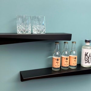 Peut inclure: Deux étagères flottantes noires contre un mur bleu sarcelle. L'étagère supérieure contient deux verres en cristal. L'étagère inférieure affiche trois bouteilles d'eau tonique et une bouteille de gin. Décoration intérieure moderne.