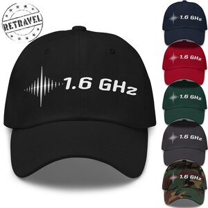 Peut inclure: Casquette de baseball noire avec l'inscription "1.6 GHz" en blanc, accompagnée d'un motif d'onde sonore blanc. L'image présente également des casquettes de couleur marine, rouge, verte, grise et camouflage.
