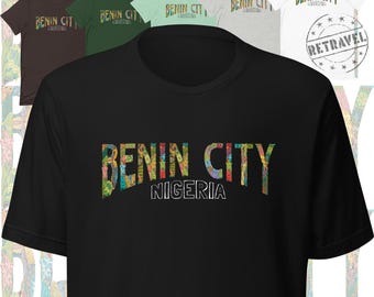 Puede incluir: Una colección de camisetas de manga corta en varios colores, incluyendo negro, marrón, verde y blanco. Cada camiseta presenta el texto "BENIN CITY NIGERIA" en una fuente colorida y estampada. Un sello "RETRAVEL" es visible en la camiseta blanca.