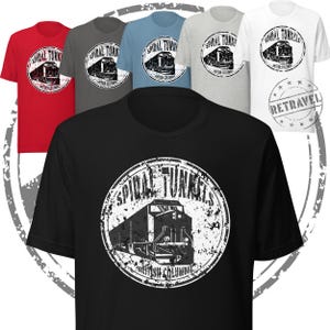 May include: A collection of short-sleeved t-shirts in various colors, including red, gray, blue, and white. Each shirt features a circular graphic with the words "Spiral Tunnels" and a train illustration. The black shirt in the foreground also displays the same design.