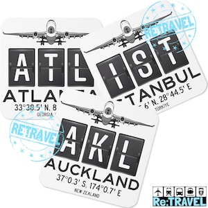 Puede incluir: Tres posavasos cuadrados blancos con gráficos en blanco y negro estilo tablero de llegadas de aeropuerto. Cada posavasos presenta un código de aeropuerto diferente: ATL para Atlanta, IST para Estambul y AKL para Auckland. Los códigos de aeropuerto se muestran en un tablero de fichas negro con un pequeño gráfico de avión sobre cada código. Las coordenadas y el país de cada aeropuerto se enumeran debajo del código de aeropuerto.