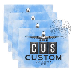 May include: Four square, light blue cloth napkins with a sky and cloud design. Each napkin features a graphic of an airplane and the word "CUSTOM" with coordinates. A "RETRAVEL" stamp is in the upper right corner.
