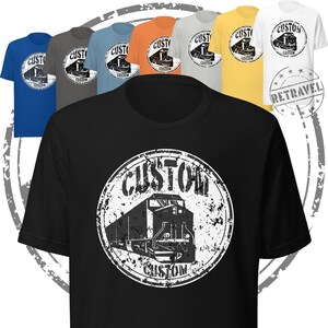 May include: A collection of t-shirts in various colors, including black, blue, gray, orange, yellow, and white. Each shirt features a distressed white graphic of a train inside a circle with the word "CUSTOM" and the word "RETRAVEL".