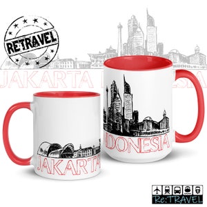 May include: Two white ceramic mugs with red rims. The mug on the left has a black and white illustration of the Jakarta skyline with the word "JAKARTA" in red text. The mug on the right has a black and white illustration of the Jakarta skyline with the words "JAKARTA INDONESIA" in red text.
