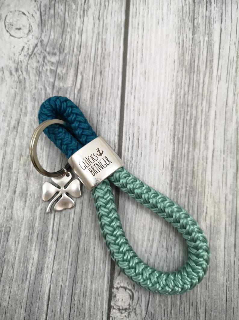 May include: Teal and green rope keychain with a silver charm that says "Gl&uuml;cksbringer" which is German for "good luck charm".