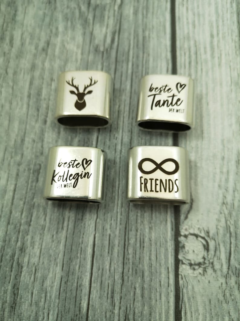 May include: Four silver charm bracelets with different engraved designs. The charms feature a deer, the words "Beste Tante der Welt", "Beste Kollegin der Welt", and "Friends" with an infinity symbol.