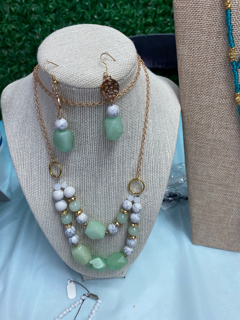 May include: A two-strand necklace with green and white beads and a matching pair of earrings. The necklace has a gold chain and the earrings have a gold charm.