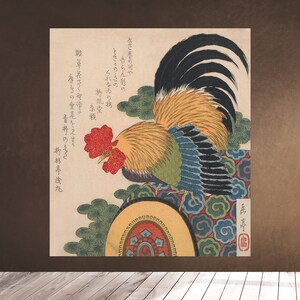 Op de afbeelding: Een traditionele Japanse houtsnede die een haan afbeeldt met een rode kam en keellap, gele en groene veren en een zwarte staart. De haan staat op een rond platform met een kleurrijk ontwerp. De print bevat Japanse tekst.