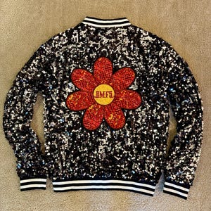 May include: Black sequined bomber jacket with a large red and yellow flower applique on the back. The flower has the letters "BMF" in the center. The jacket has white and black striped trim on the collar, cuffs, and hem.