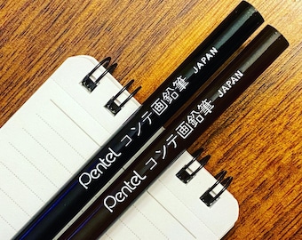 May include: Two black Pentel pens with white lettering that reads "Pentel コンテ画鉛筆" and "JAPAN".