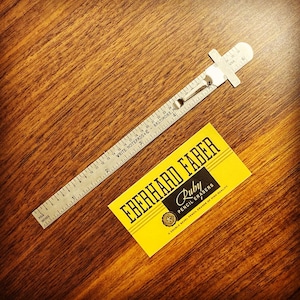 Puede incluir: Un paquete de gomas de borrar para lápices Eberhard Faber amarillo y negro con el texto "Ruby Pencil Erasers" y "A double bevel pencil eraser of high quality". También se ve una regla plateada con el texto "Write Notepads Baltimore, Md."