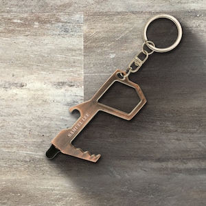 May include: A copper-colored key chain tool with a bottle opener, a stylus, and a loop for a key ring. The tool is engraved with the text "SAMUEL LEE".