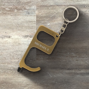 May include: Gold-coloured door opener keychain with a stylus tip and a loop for a key ring. The keychain is engraved with the name "MICHAEL T."