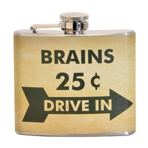 Puede incluir: Una petaca de acero inoxidable con una tapa plateada y una etiqueta de estilo vintage que dice "BRAINS 25¢ DRIVE IN" en texto negro y verde sobre un fondo beige.
