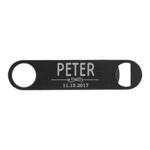 May include: Black bottle opener with a circular hole on one end and a bottle cap opener on the other. The word "PETER" is engraved in white, along with the date "11.15.2017".