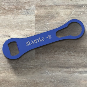 Puede incluir: Abrebotellas de metal azul con un trébol y el texto "GEORGE 3/7/18" y "sláinte" impreso en él.