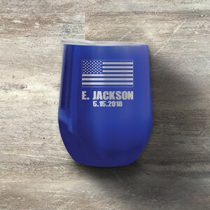 以下が含まれることがあります： 銀色のアメリカ国旗と「E. JACKSON 5.15.2018」という文字が刻まれた、青いステンレス製のワインタンブラーです。