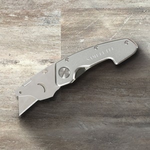 May include: A silver utility knife with a retractable blade and a handle that says "SAMUEL LEE".