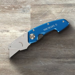 May include: A blue utility knife with a silver blade and a personalized inscription that reads "MICHAEL T."