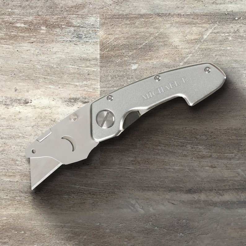 May include: A silver utility knife with a retractable blade and a personalized inscription that reads "MICHAEL T."