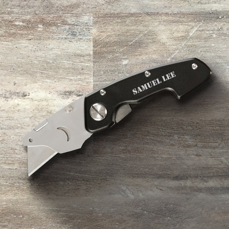 May include: A black utility knife with a silver blade and a personalized inscription that reads "SAMUEL LEE".