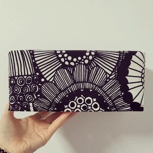 May include: Black and white patterned fabric clutch with a geometric design. The fabric features a repeating pattern of circles, lines, and swirls.