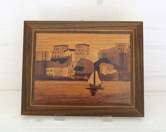 Wooden inlay painting depicting a seascape with boat and houses in the background