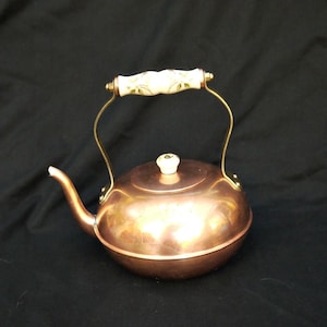 May include: A copper kettle with a white ceramic handle and knob. The kettle has a shiny, polished finish.
