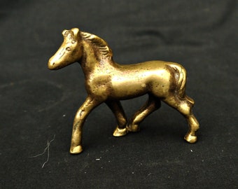 May include: A small, gold-colored metal horse figurine. The horse is standing on all four legs and has its head turned to the left. The figurine is about 3 inches tall.