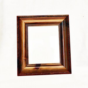 May include: A dark brown wooden picture frame with a simple, ornate design. The frame is empty and ready to hold a photo or artwork.