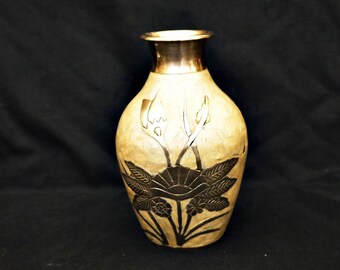 May include: A cream-colored ceramic vase with a gold rim and a silver floral design. The vase has a rounded body and a narrow neck.
