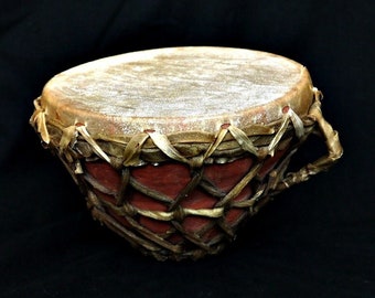 May include: A brown and red drum with a woven design. The drum is made of wood and has a leather head.