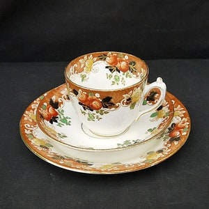 May include: A white teacup and saucer set with a floral pattern in shades of orange, green, and yellow. The cup and saucer have a gold trim.
