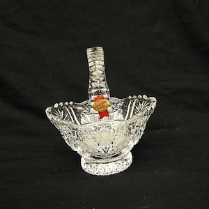 May include: A clear glass bowl with a cut glass design and a handle. The bowl has a label that reads "Lenox, Made in Czechoslovakia".