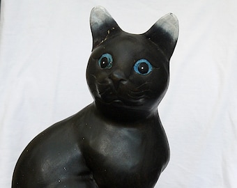 Puede incluir: Figura de gato de cerámica negra con ojos azules, sentada sobre un encaje blanco de ganchillo con un centro morado.