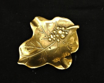 May include: A gold-colored metal leaf-shaped trinket dish with a grape design.