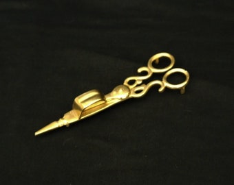May include: A gold-colored metal scissor-shaped candle snuffer with a pointed end.