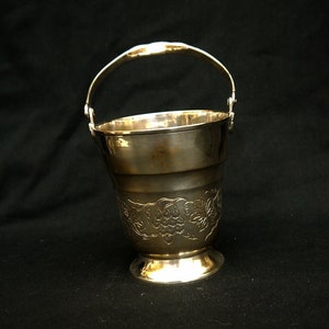 May include: Silver ice bucket with a decorative grape design and a handle. The bucket is on a black background.