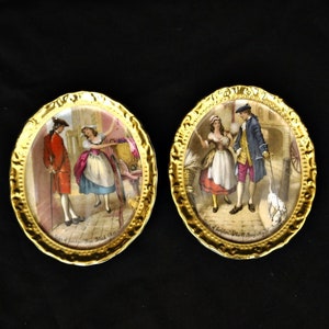Puede incluir: Dos platos ovalados de porcelana con ribetes dorados y escenas pintadas. Los platos representan a un hombre y una mujer con ropa del siglo XVIII. El texto en los platos dice "The Jealous Wife" y "The Country Girl".