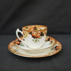 May include: A vintage teacup and saucer set with a floral pattern in shades of orange, brown, green, and black. The cup and saucer have a gold trim.