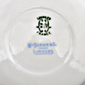 Puede incluir: Primer plano de la parte inferior de un platillo de porcelana blanca con un logotipo verde y negro que dice "Limoges France" y una inscripci&oacute;n azul que dice "W. Goerz & Co. Limoges".
