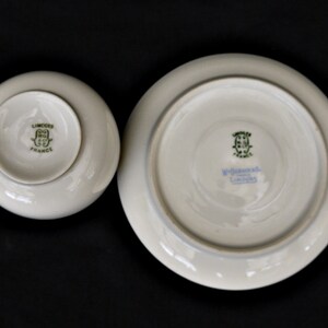 Puede incluir: Un juego de taza y platillo de porcelana blanca con marcas verdes y doradas. El platillo tiene el texto "W. Goebel, Limoges" y la taza tiene el texto "Limoges, France".