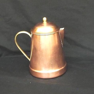 May include: A copper teapot with a brass handle and a shiny finish. The teapot has a rounded body and a lid with a knob on top.