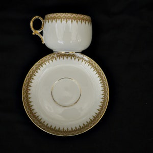 Puede incluir: Un juego de taza y platillo de t&eacute; blanco con borde dorado y un patr&oacute;n floral verde y dorado.