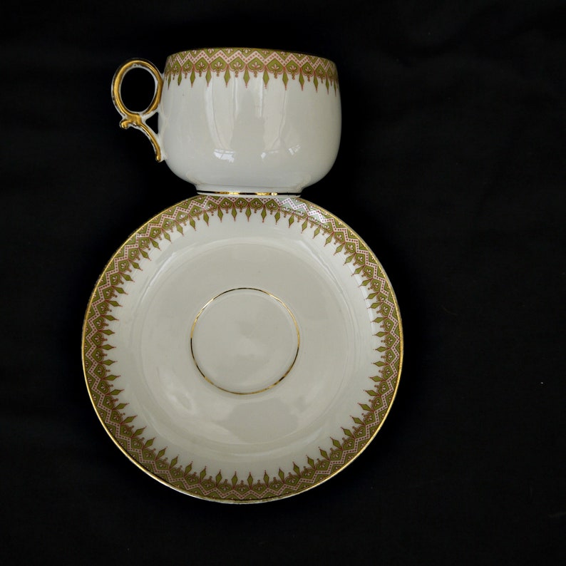 Puede incluir: Un juego de taza y platillo de t&eacute; blanco con borde dorado y un patr&oacute;n floral verde y dorado.