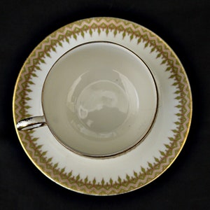 Puede incluir: Una taza de t&eacute; y un platillo blancos con un patr&oacute;n floral verde y dorado alrededor del borde.