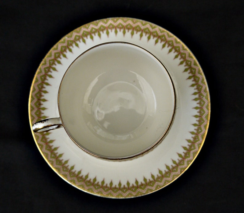 Puede incluir: Una taza de t&eacute; y un platillo blancos con un patr&oacute;n floral verde y dorado alrededor del borde.