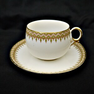 Puede incluir: Una taza de t&eacute; y un platillo blancos con un patr&oacute;n floral verde y rosa y un borde dorado.